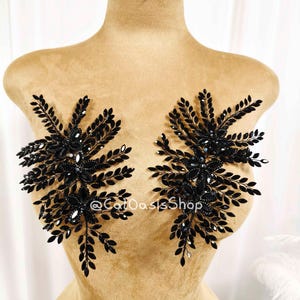 May include: Two black beaded floral appliques with a leaf design are displayed on a mannequin. The appliques are embellished with small, sparkling crystals. The text "@CatOasisShop" is visible on the mannequin.