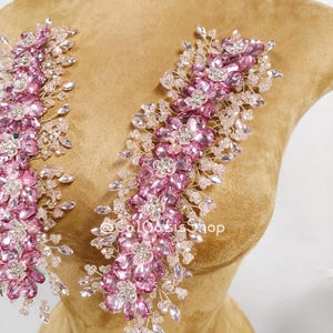 May include: Two elongated floral appliques featuring pink faceted crystals arranged in flower shapes, accented with clear crystal beads on thin silver-toned wire branches. The text @CalOasisShop is visible in white lettering between the two pieces.