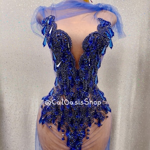 May include: A sheer blue fabric bodice with a deep V-neckline, embellished with blue rhinestones and crystals. The bodice is on a mannequin and has the text "@CalOasisShop" on the front.