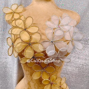 Puede incluir: Dos juegos de adornos con forma de flor, uno en dorado y otro en plateado, con pedrería. Los adornos están en un torso de maniquí marrón. El texto "@CalOasisShop" es visible en el maniquí.