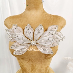May include: A white fabric applique shaped like a cluster of leaves, embellished with clear rhinestones and silver beading along the edges and veins. The piece features the text @CalOasisShop printed in white across the center of the design.