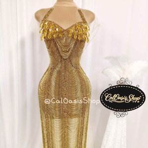 Könnte beinhalten: Ein goldfarbenes, bodenlanges Kleid mit Neckholder-Ausschnitt. Das Oberteil ist mit glitzernden goldenen Steinen und Perlenfransen verziert. Das Kleid besteht aus goldfarbenen Ketten und Perlen und erzeugt eine fließende, elegante Silhouette.