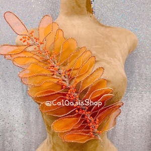 May include: An orange fabric leaf and berry embellishment with a beaded edge is displayed on a mannequin. The design features a central stem with small orange berries and the text "@CaLOasisShop".