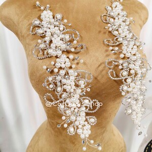 May include: Two elongated decorative appliqués featuring a dense arrangement of white faux pearls and clear rhinestones set on silver-toned wire. The intricate, swirling floral-inspired design creates a symmetrical pattern of beaded embellishments.