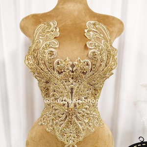 May include: A gold-colored, ornate bodice applique with intricate beadwork and a floral design. The applique is displayed on a mannequin, showcasing its detailed craftsmanship and potential for embellishing garments.