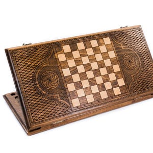 May include: A wooden backgammon and chess board combination. The board is made of dark brown wood with a checkerboard pattern in the center. Intricate carvings and decorative patterns adorn the edges, adding a touch of elegance to this classic game set.