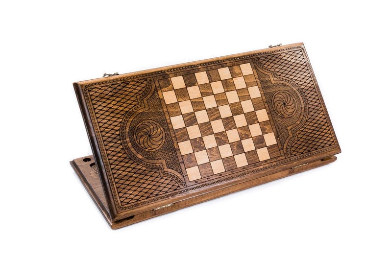 May include: A wooden backgammon and chess board combination. The board is made of dark brown wood with a checkerboard pattern in the center. Intricate carvings and decorative patterns adorn the edges, adding a touch of elegance to this classic game set.