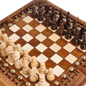May include: A wooden chess set with a checkered board and intricately carved border. The chess pieces are dark brown and light beige, arranged on the board. Brass accents are visible around the border.