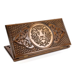 May include: A wooden game box with an intricate design featuring a lion's head in the center. The box is closed and has a dark brown finish.