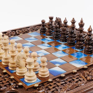 May include: A wooden chess set with intricately carved detailing around the board's perimeter. The chessboard features alternating squares of brown wood and blue-and-white patterned tiles. The chess pieces are light and dark wood.