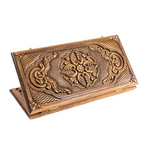 May include: A wooden backgammon set with intricate floral carvings. The set is a warm brown color, with detailed relief patterns on the lid. The game board is open, revealing the interior.