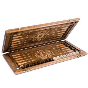 May include: Wooden backgammon set, open to display the playing surface. The board is brown with inlaid light wood triangles and circular carvings. Includes light and dark game pieces. The set is made of wood.