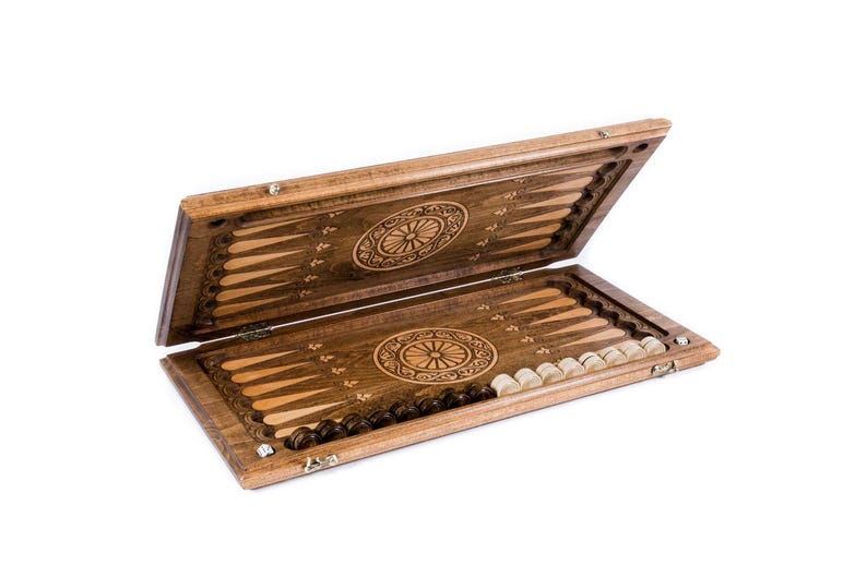May include: Wooden backgammon set, open to display the playing surface. The board is brown with inlaid light wood triangles and circular carvings. Includes light and dark game pieces. The set is made of wood.