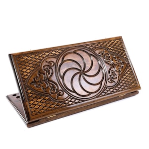 May include: Wooden backgammon board with intricate carved designs. The board is a rich brown color, featuring a central spiral motif and detailed geometric patterns. The game board is open, displaying the playing surface.
