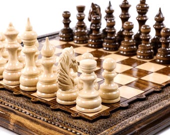 May include: A wooden chess set with light and dark pieces arranged on a checkered board. The chess pieces are intricately carved, with a knight piece prominently displayed. The board has a decorative border.