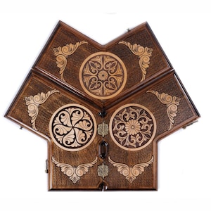 May include: A wooden backgammon board with a unique star-like shape. The board is made of dark brown wood with intricate, light-colored floral and geometric designs. The board is divided into sections and has metal hinges and clasps.