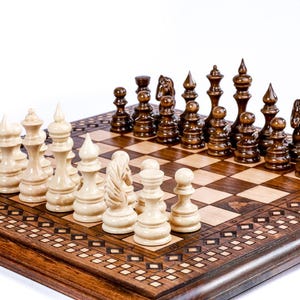May include: A wooden chess set with light and dark pieces arranged on a checkered board. The board is set in a decorative wooden frame with inlaid patterns. The chess pieces are carved in a classic style.