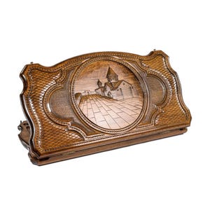 May include: A wooden backgammon board with intricate carvings. The center features a detailed relief of a building with a domed roof and a paved pathway. The board is a warm brown color and has a textured, patterned border.