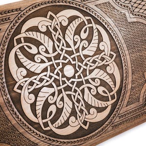 May include: Wooden decorative panel featuring a detailed Celtic knotwork design. The central circular motif showcases interwoven patterns, framed by a decorative border and geometric corner designs. The wood has a warm, natural tone, with lighter carved details.