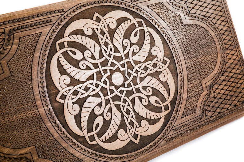 May include: Wooden decorative panel featuring a detailed Celtic knotwork design. The central circular motif showcases interwoven patterns, framed by a decorative border and geometric corner designs. The wood has a warm, natural tone, with lighter carved details.
