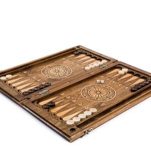 May include: A wooden backgammon board with a detailed, carved design. The board is brown with light and dark wood accents, and includes white and black game pieces, and dice. The game board is open and ready for play.