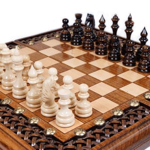 May include: A wooden chess set with light and dark pieces arranged on a checkered board. The board is framed with a decorative border and brass accents. The chess pieces are in the starting positions, ready for a game.