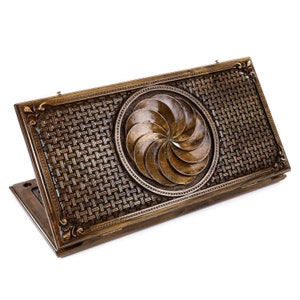 May include: A wooden game board with a carved design of a swirling pattern in a circle. The board is closed and has a brown finish.