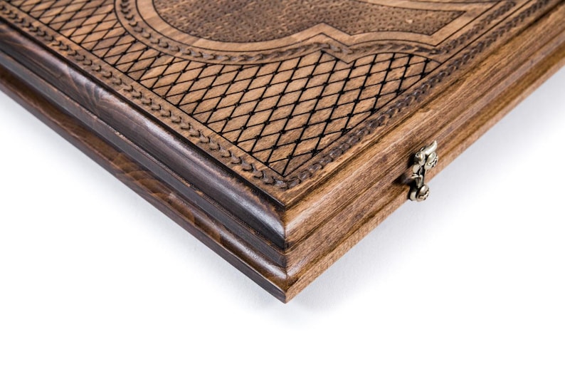 May include: Close-up of a wooden backgammon board. The board is made of light and dark brown wood with intricate carved details. The edges are dark brown, and the surface features a diamond pattern and decorative borders.