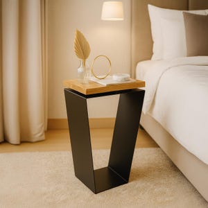 May include: A modern side table with a black metal base and a natural wood top. The table is in a bedroom setting and has decorative items on top, including a vase, a gold ring, and a small marble object. The table is approximately 24 inches tall.