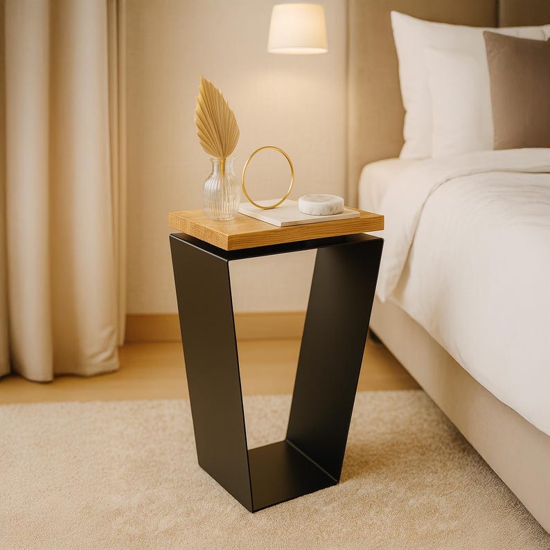 May include: A modern side table with a black metal base and a natural wood top. The table is in a bedroom setting and has decorative items on top, including a vase, a gold ring, and a small marble object. The table is approximately 24 inches tall.
