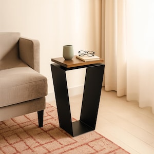 May include: A modern side table with a black metal base and a two-tiered top. The top tier is a dark wood, and the bottom tier is black. A small green vase, a pair of glasses, and a book rest on the table.