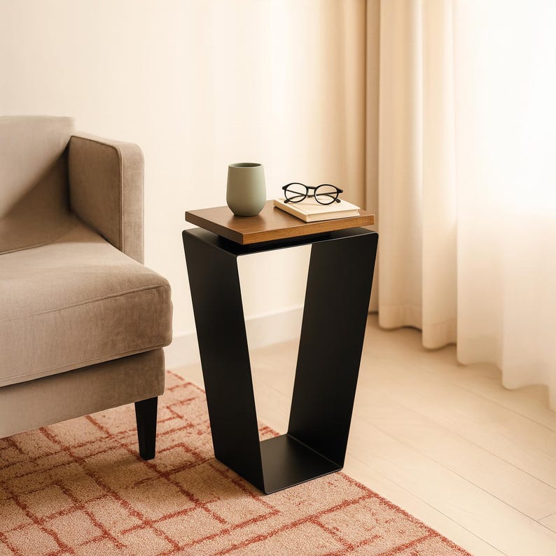 May include: A modern side table with a black metal base and a two-tiered top. The top tier is a dark wood, and the bottom tier is black. A small green vase, a pair of glasses, and a book rest on the table.