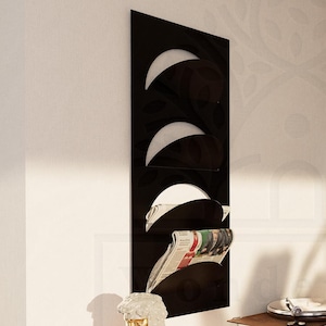 May include: A black metal magazine rack with three curved compartments, holding rolled up newspapers. The rack is mounted on a white wall next to a yellow dresser with a record player on top.