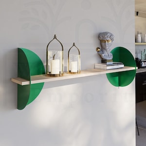 以下が含まれることがあります： 明るい木製の板と緑色の半円形のサポートを備えたモダンな壁棚。 棚には、ガラスホルダーに入ったキャンドルや胸像の彫刻など、装飾品が飾られています。 棚は明るい灰色の壁に取り付けられています。