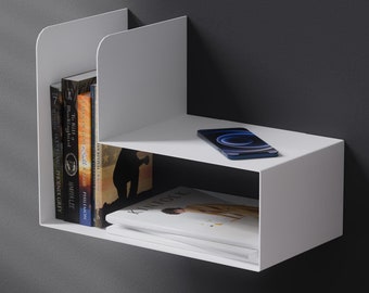 May include: White wall mounted shelf with two shelves. The top shelf has a black cell phone on it. The bottom shelf has a stack of books and a magazine.