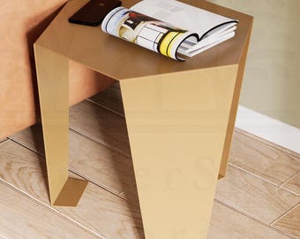 May include: A modern, gold-colored side table with a geometric design. The table has an angled top and legs, and is next to a tan leather sofa. A magazine and a smartphone rest on the table's surface. The floor is made of light-colored wood.
