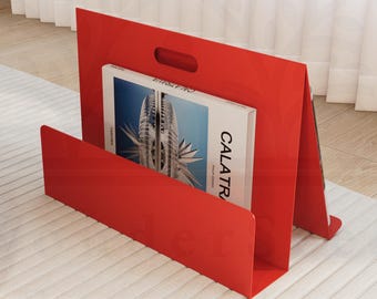 Könnte beinhalten: Ein roter Magazinhalter aus Metall mit einem Magazin mit dem Titel "CALATRAVA" darin. Der Halter steht auf einem weißen Teppich.