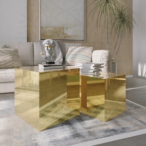 May include: Two gold mirrored square coffee tables with a sculpture of a man's head on top of one table. The tables are in front of a white sofa with cushions and a painting on the wall behind the sofa.