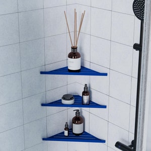 May include: Three blue corner shelves in a white tiled shower with various bottles and a jar of lotion. The top shelf has a bottle of diffuser oil with sticks. The middle shelf has a bottle of lotion. The bottom shelf has a bottle of lotion and a small bottle of oil.
