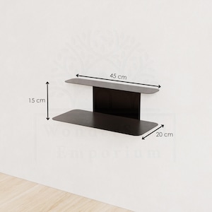 May include: A black metal wall shelf. The shelf is 45 cm wide, 15 cm high, and 20 cm deep. The shelf has a modern design and is mounted on a white wall. The shelf is empty.