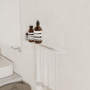 May include: A white acrylic bathroom shelf with a towel rail, holding three brown bottles with white labels. A white towel with a grey stripe hangs from the rail. The shelf is mounted on a white wall.
