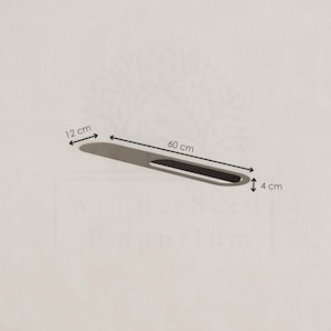 May include: A silver-coloured, elongated object with a black, oval-shaped cutout. The object is 60 cm long, 12 cm wide, and 4 cm thick. The object is on a light beige background.