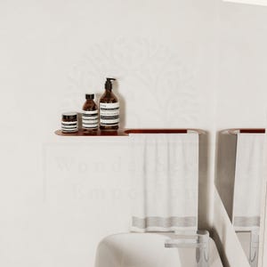 May include: A bathroom shelf with three brown bottles and a small jar. The shelf is made of dark wood and is mounted on a white wall. Below the shelf are two white towels with grey stripes. The image has a minimalist aesthetic.
