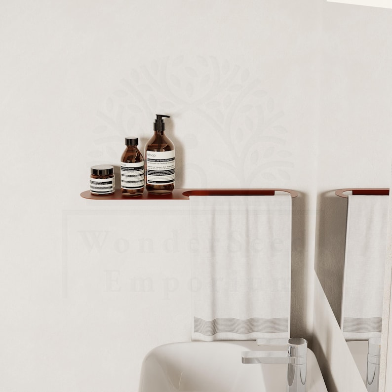 May include: A bathroom shelf with three brown bottles and a small jar. The shelf is made of dark wood and is mounted on a white wall. Below the shelf are two white towels with grey stripes. The image has a minimalist aesthetic.