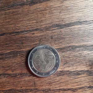 May include: A silver Euro coin with a design featuring a depiction of the European Union flag and the text "2002" and "EUROPA" on the coin.