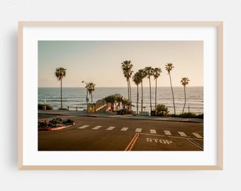 May include: A framed photograph of a coastal scene featuring palm trees, a road, and the ocean. The image has a warm, golden hue, with the sun setting over the water. The word "STOP" is visible on the road.