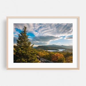 Puede incluir: Impresión enmarcada de un paisaje con una vista panorámica de un lago rodeado de montañas y colorido follaje otoñal. Un árbol de hoja perenne alto está en primer plano, bajo un cielo azul nublado.