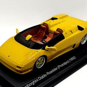 Könnte beinhalten: Ein gelbes Lamborghini Diablo Roadster (Prototipo) Modell im Maßstab 1:18. Das Auto ist ein Cabriolet mit schwarzem Innenraum und schwarzer Windschutzscheibe. Das Auto steht auf einem schwarzen Display-Sockel mit dem Text "Lamborghini Diablo Roadster (Prototipo) (1992)" und "1 von 1.000".