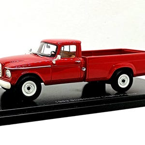 Könnte beinhalten: Ein rotes 1963 Studebaker Champ Pickup-Modellauto mit weißer Frontstoßstange, weißen Rädern und schwarzem Innenraum. Das Fahrzeug ist auf einem schwarzen rechteckigen Sockel mit der Aufschrift 1963 Studebaker Champ Pickup montiert.