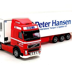 Peut inclure: Maquette de camion rouge et blanc Peter Hansen International Transport & Spedition A/S. La cabine rouge porte l'inscription "H.P. THERKELSEN", la remorque blanche le nom de l'entreprise en bleu. Il comprend une unité de réfrigération Thermo King.